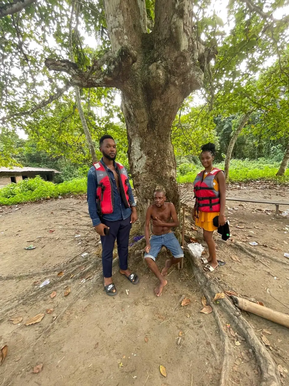 Des visiteurs et un habitant au pied d'un grand arbre du campement