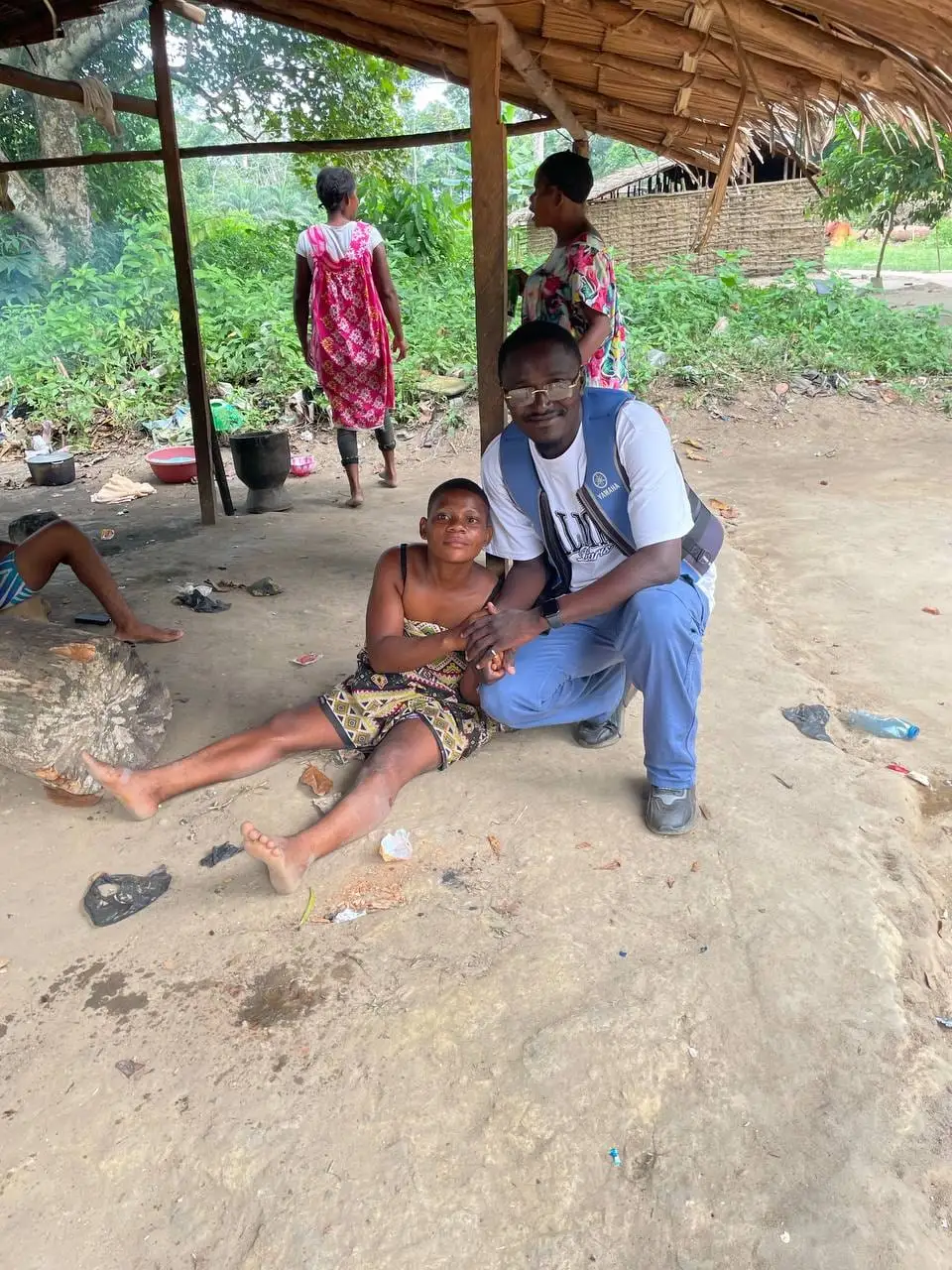 Un visiteur accroupi auprès d'une habitante, sous un abri du campement