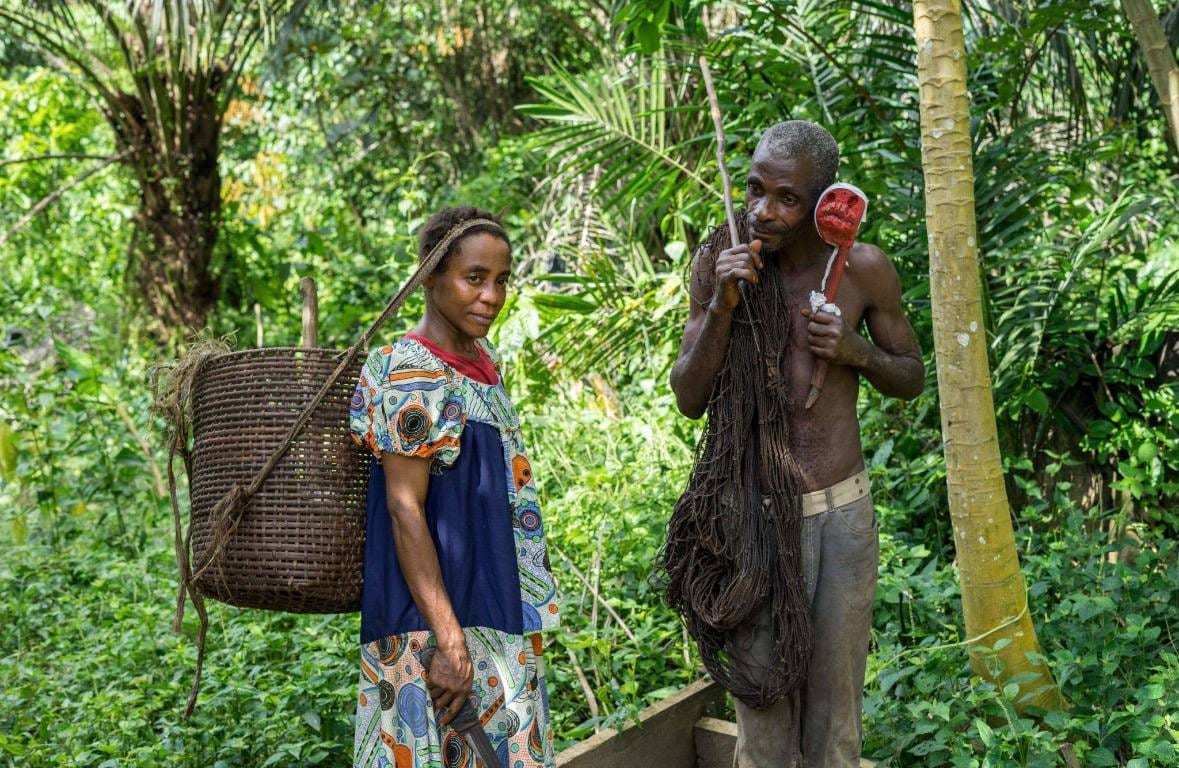 Un couple bagyeli en forêt, elle avec une hotte tressée, lui avec un filet de chasse