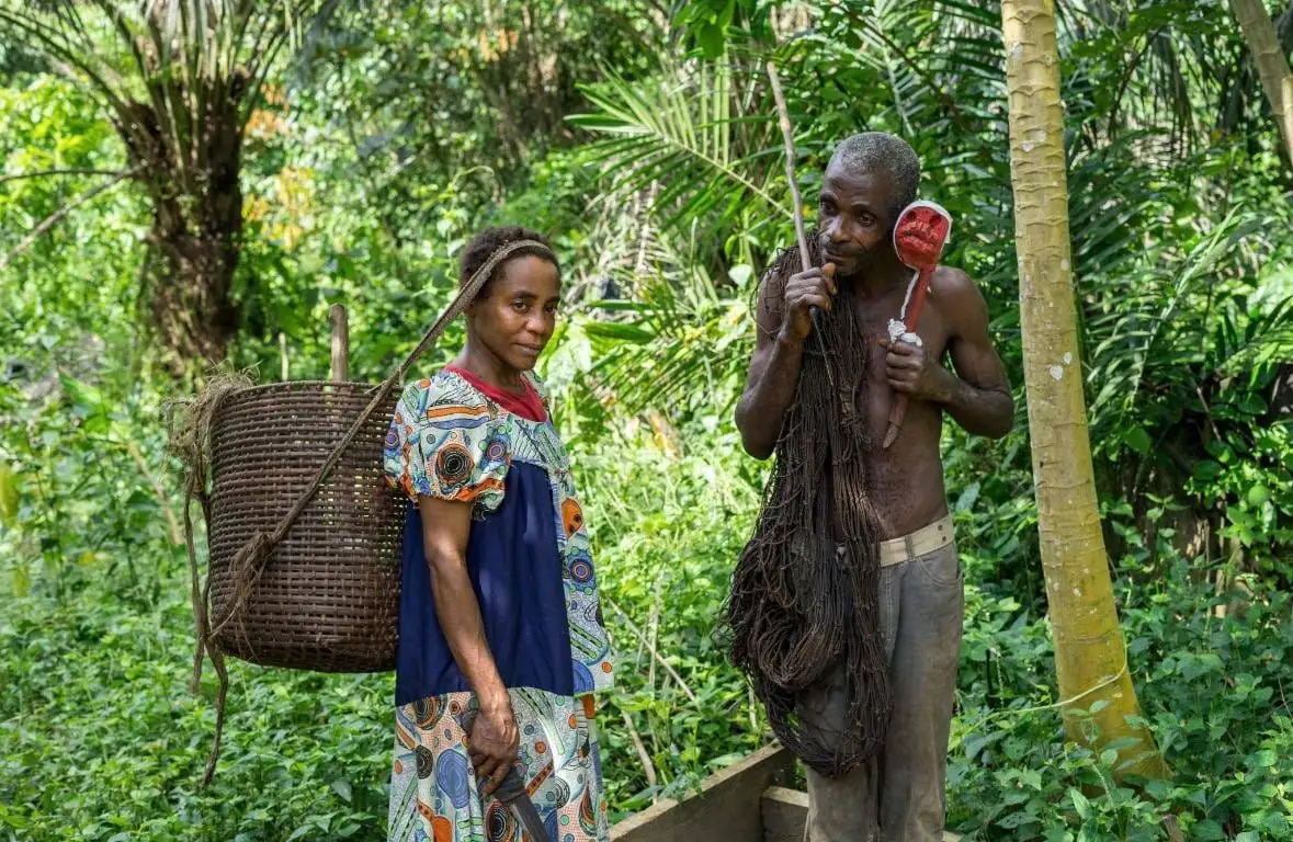 Un couple bagyeli en forêt, elle avec une hotte tressée, lui avec un filet de chasse