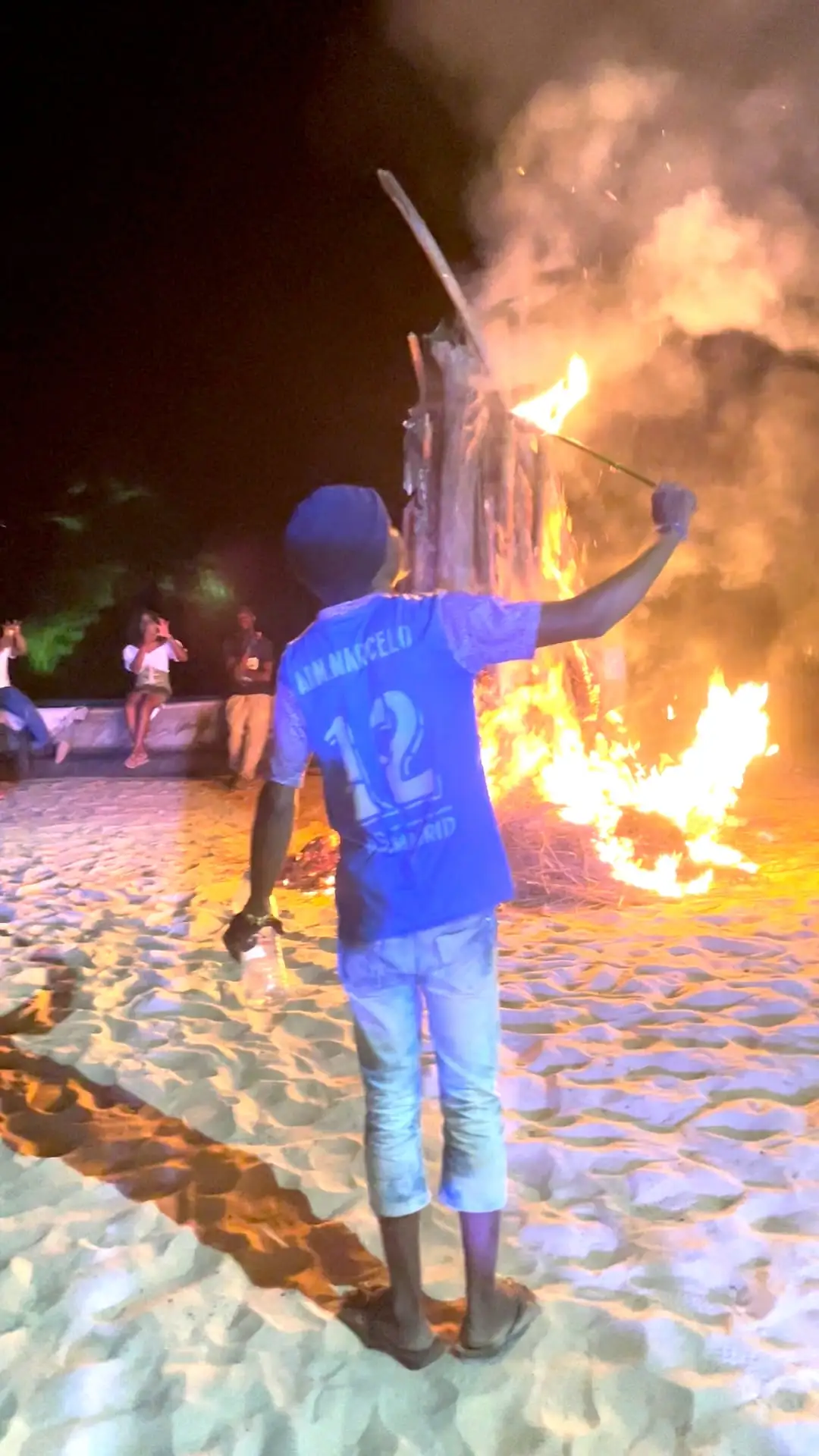 Un homme près d’un grand feu de bois, la nuit sur la plage
