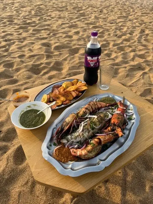 Un plateau de gambas grillées servi sur une table basse, sur le sable