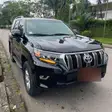 Un Toyota Land Cruiser Prado noir garé au bord d'une route bordée de palmiers