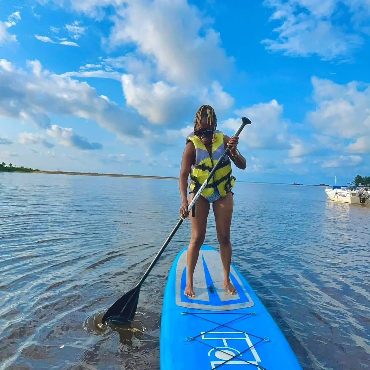 Une femme debout sur une planche de paddle, sous un ciel bleu