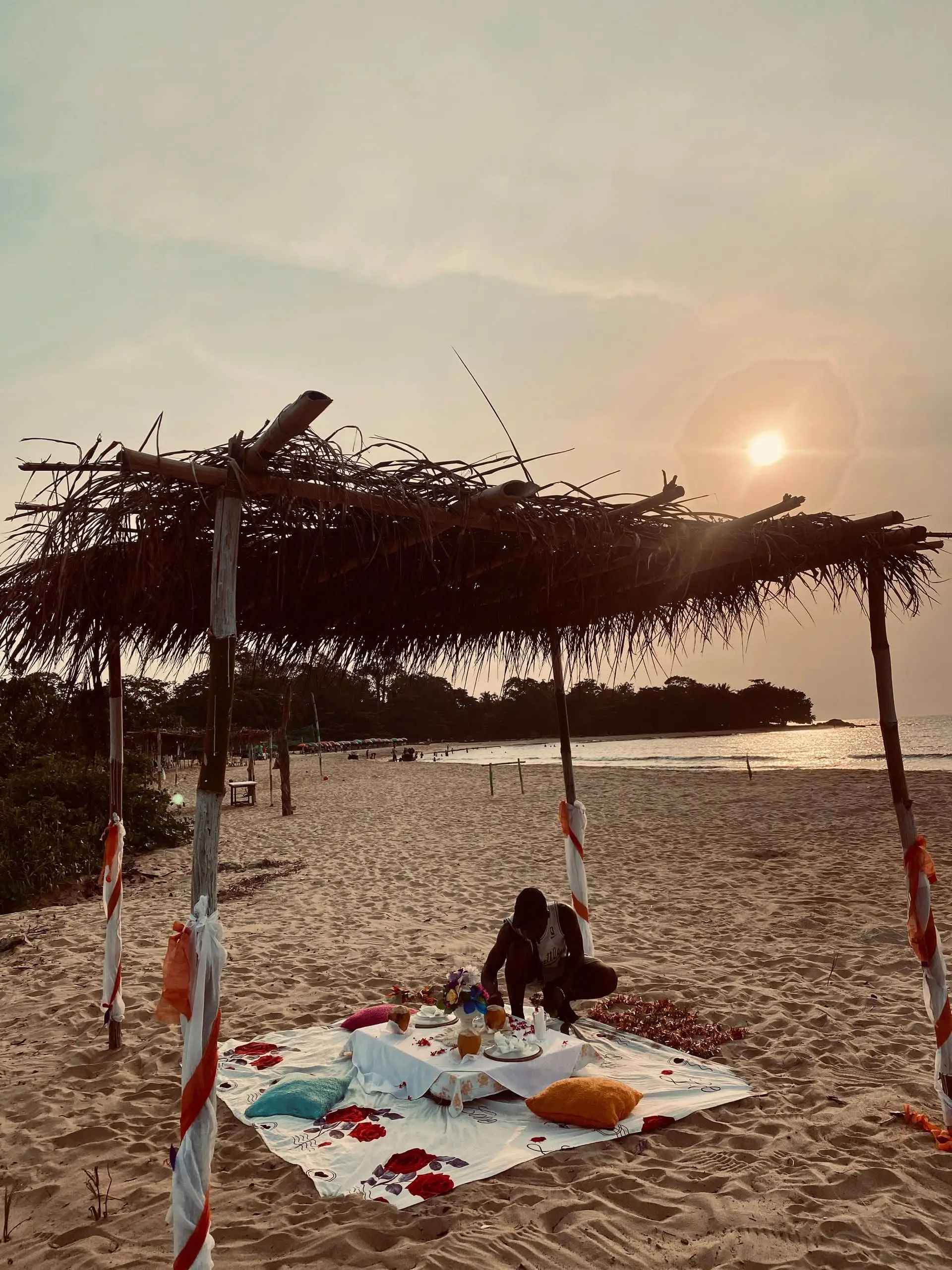 Un pique-nique installé sous une paillote, sur la plage au coucher du soleil