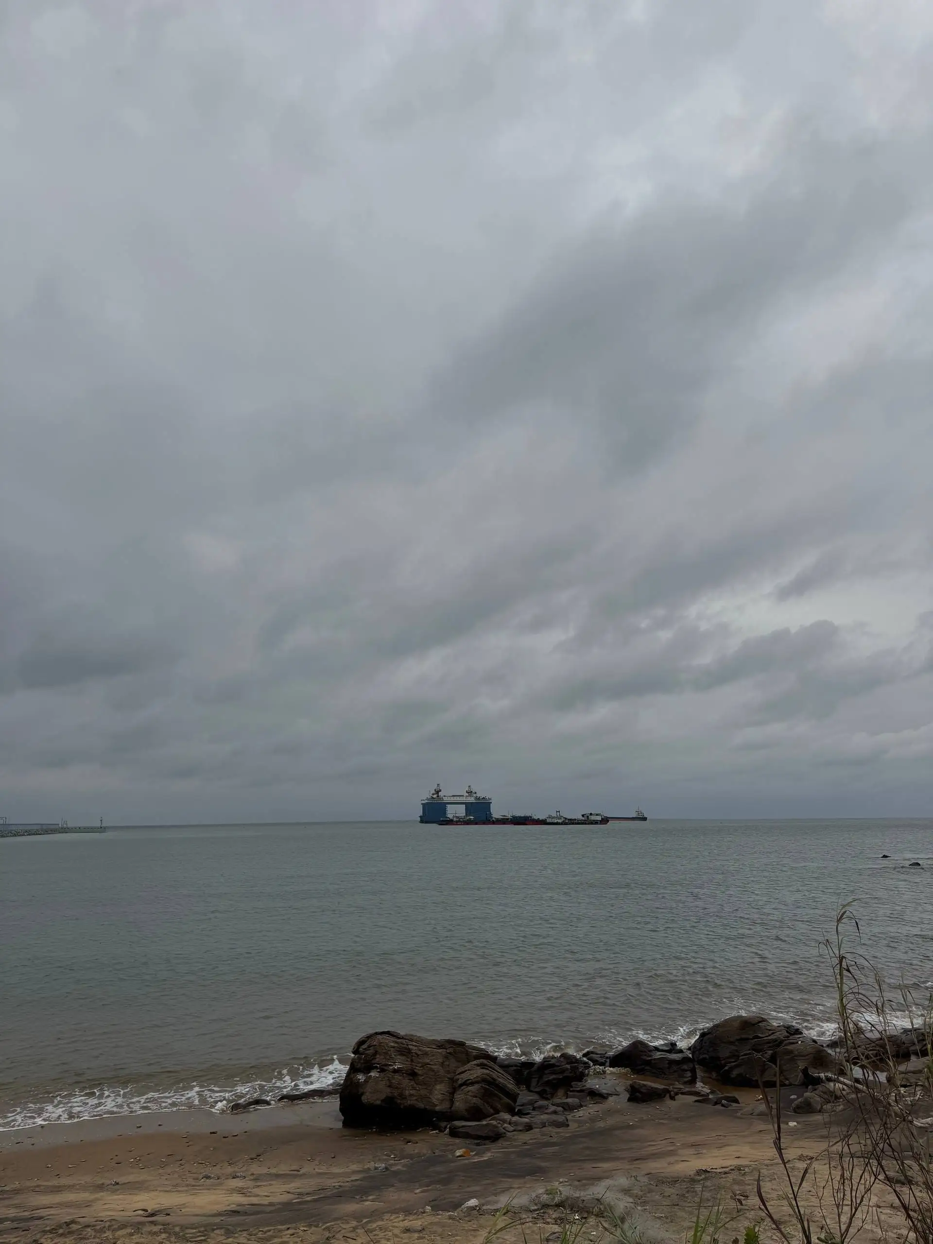 Un navire et des barges au large, vus depuis une plage de rochers