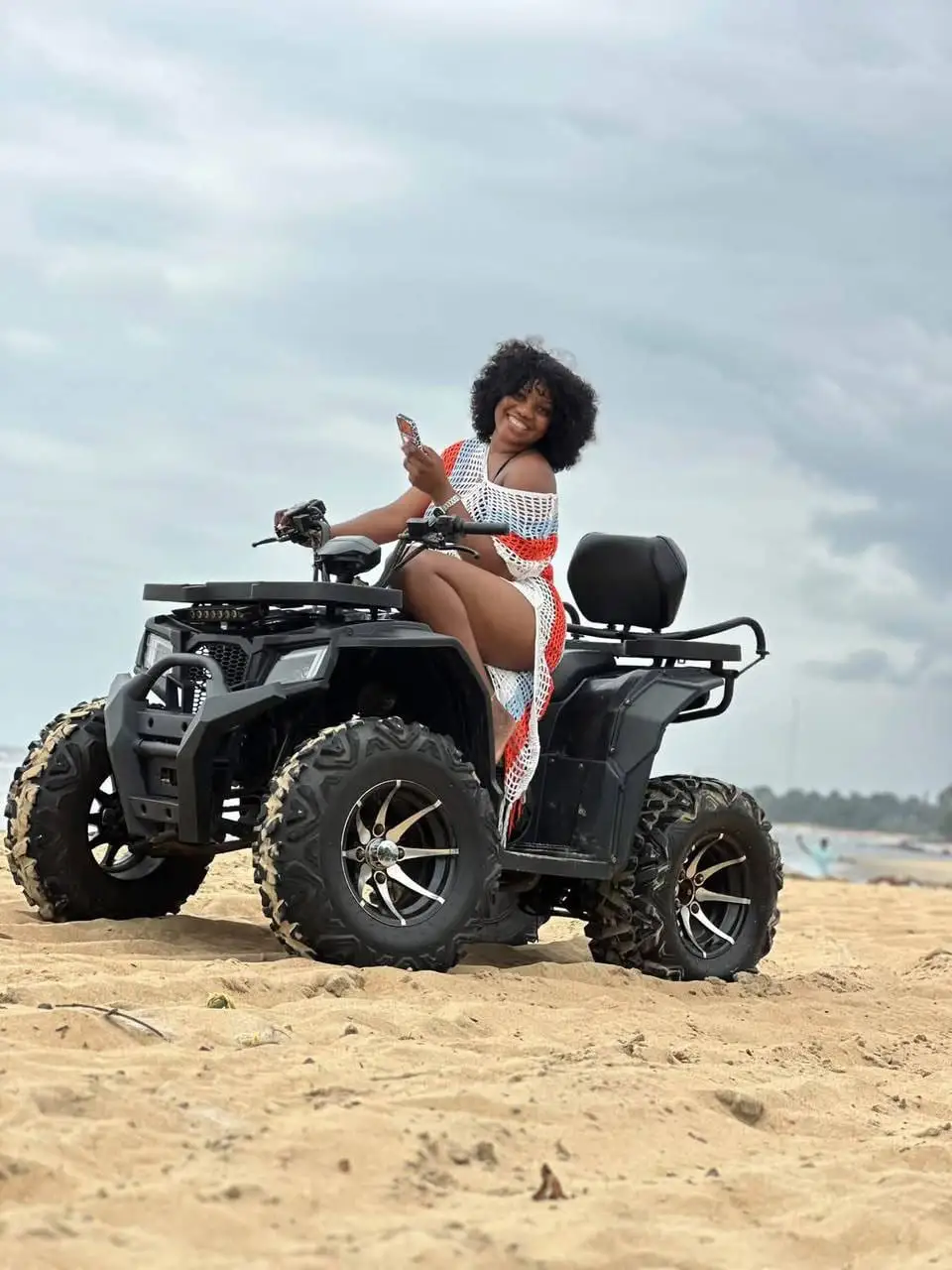 Une jeune femme pose sur un quad, sur la plage
