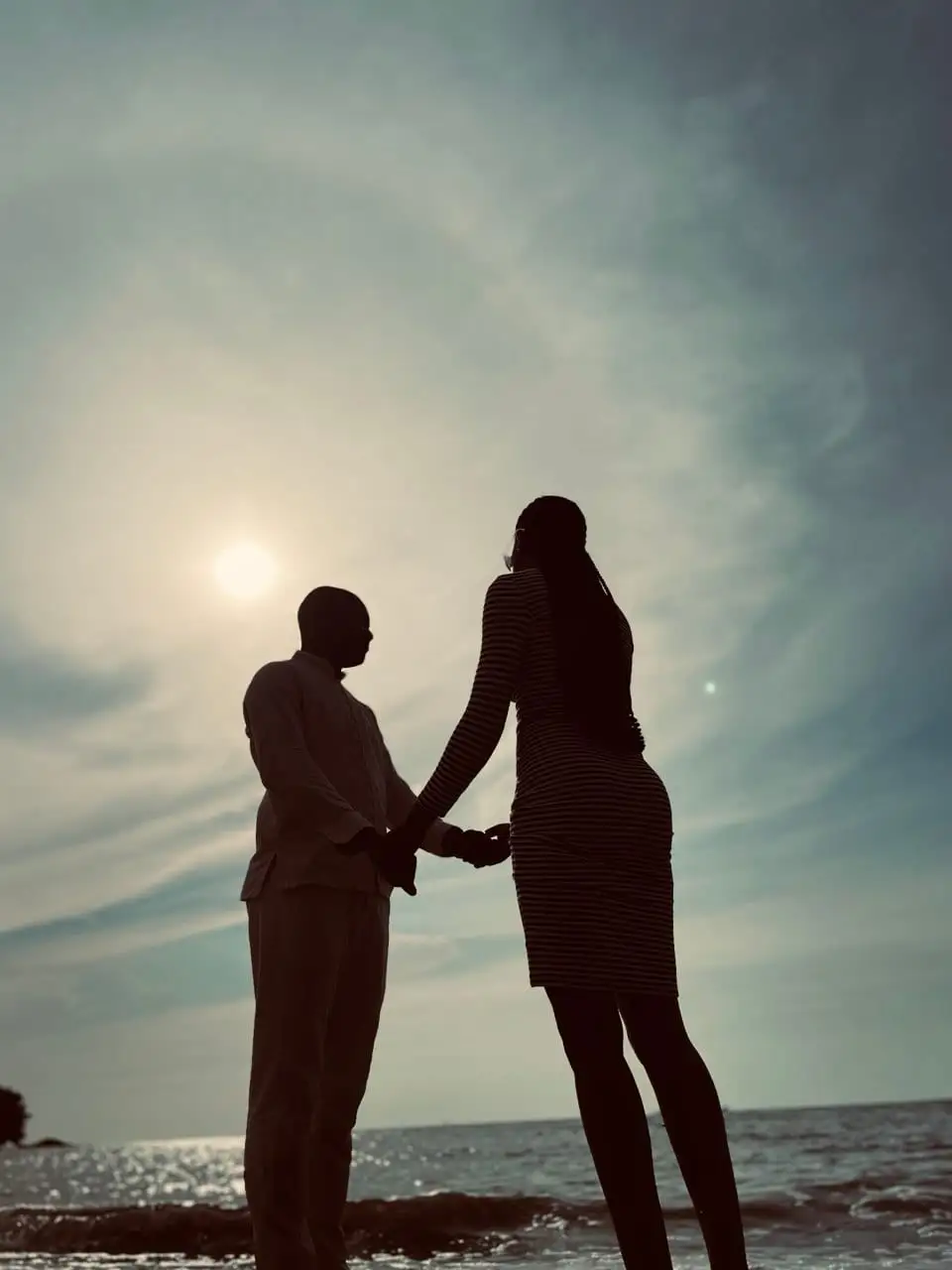 Silhouettes d'un couple main dans la main, face au soleil voilé sur la mer